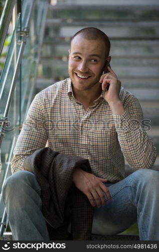 Businessman sitting on stairs at office building and talking by phone