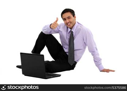 businessman sitting on the floor with his laptop and making a thumbs up sign