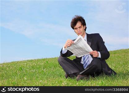 businessman sitting on the meadow and reading newspaper