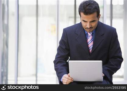 Businessman sitting outdoors by building with a laptop (high key/selective focus)