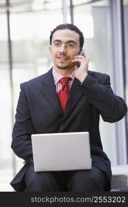 Businessman sitting outdoors by building with a laptop on cellular phone (high key/selective focus)