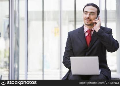 Businessman sitting outdoors by building with a laptop on cellular phone (high key/selective focus)