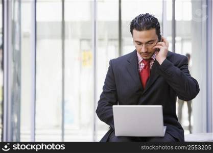 Businessman sitting outdoors by building with a laptop on cellular phone (high key/selective focus)