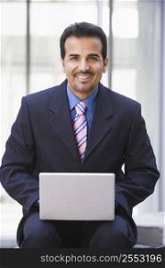 Businessman sitting outdoors by building with a laptop smiling (high key/selective focus)
