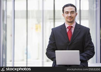 Businessman sitting outdoors by building with a laptop smiling (high key/selective focus)