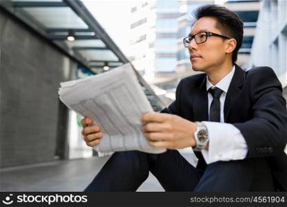Businessman sitting outdoors with newspaper. First news in the morning