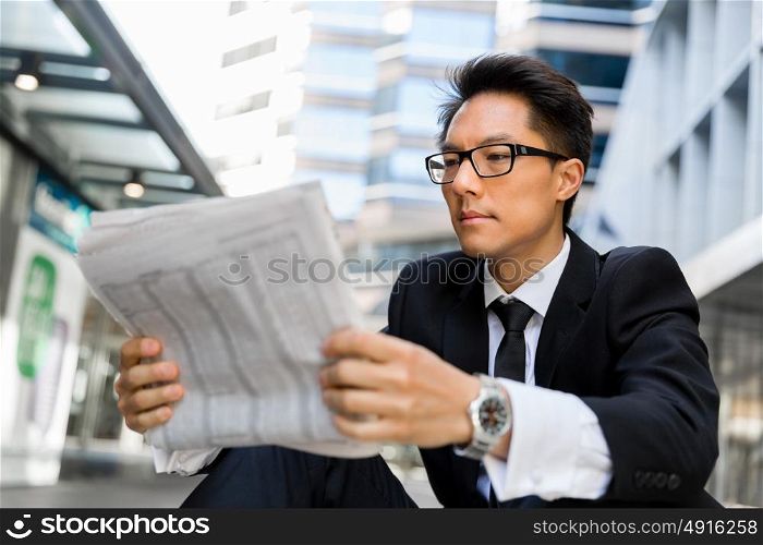 Businessman sitting outdoors with newspaper. First news in the morning