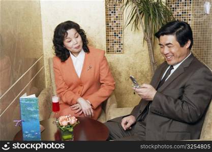 Businessman sitting with a businesswoman in a restaurant looking at a mobile phone