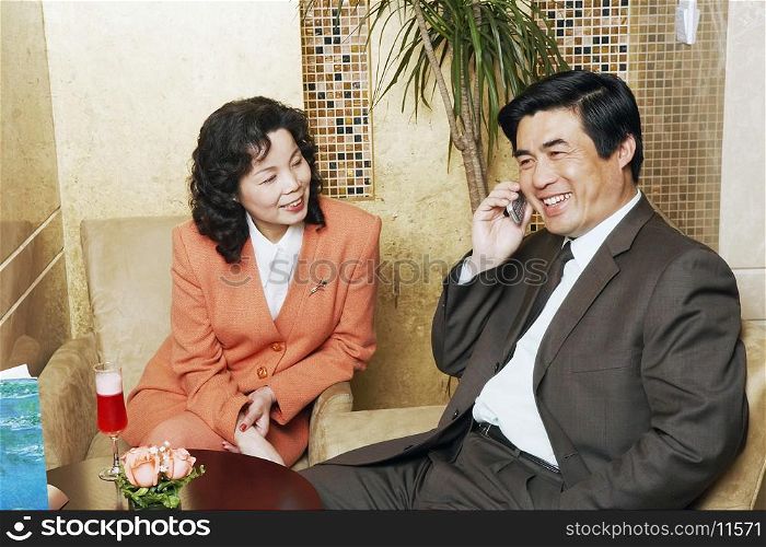 Businessman sitting with a businesswoman in a restaurant talking on a mobile phone