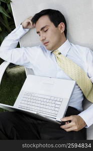 Businessman sleeping on a lounge chair with a laptop on his lap