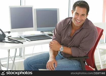 Businessman smiling by computers in office portrait