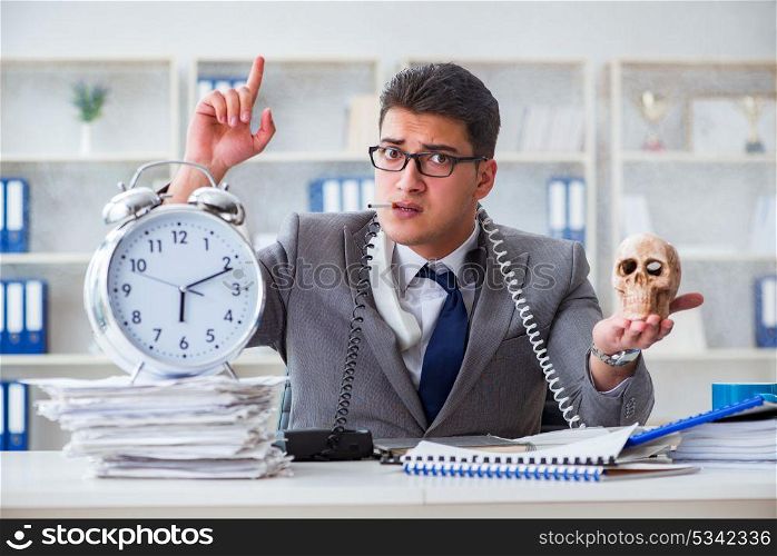 Businessman smoking holding human skull and an alarm clock in th. Businessman smoking holding human skull and an alarm clock in the office