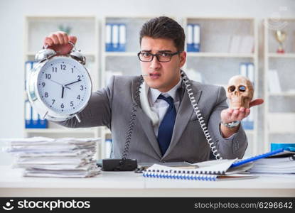 Businessman smoking holding human skull and an alarm clock in th. Businessman smoking holding human skull and an alarm clock in the office