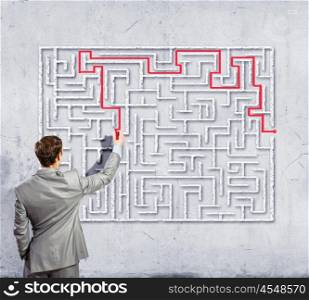 Businessman solving labyrinth problem. Back view image of young businessman trying to find way out of maze