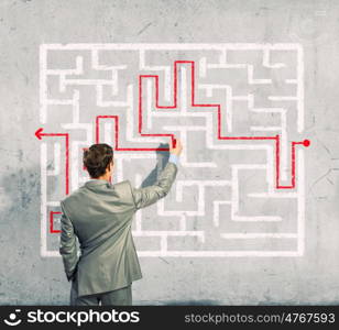 Businessman solving labyrinth problem. Back view image of young businessman trying to find way out of maze