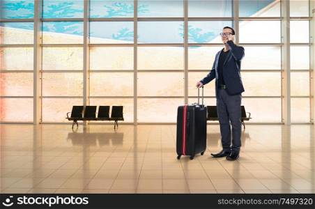 Businessman speaking on phone and carrying suitcase in airport waiting lounge
