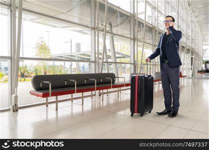 Businessman speaking on phone and carrying suitcase in airport waiting lounge