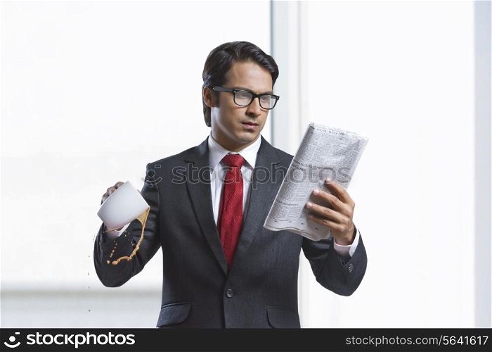 Businessman spilling coffee while reading newspaper in office