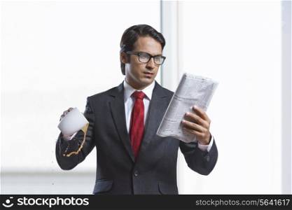 Businessman spilling coffee while reading newspaper in office