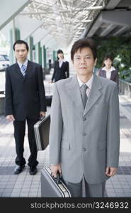 Businessman standing and holding his suitcase with three business executives in the background