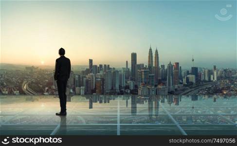Businessman standing at transparent glass floor on rooftop with city skyline, success and thinking concept .