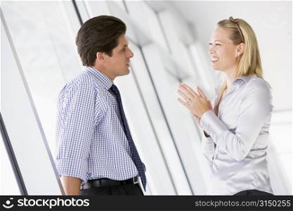 Businessman standing in corridor talking to smiling businesswoman