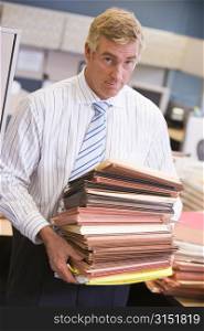 Businessman standing in cubicle with stacks of files