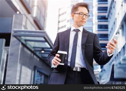 Businessman standing in street and looking at his phone. No minute wasted