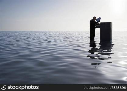 Businessman Standing in the Ocean Searching Through a Filing Cabinet