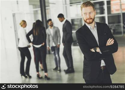Businessman standing in the office and other business people talking at background