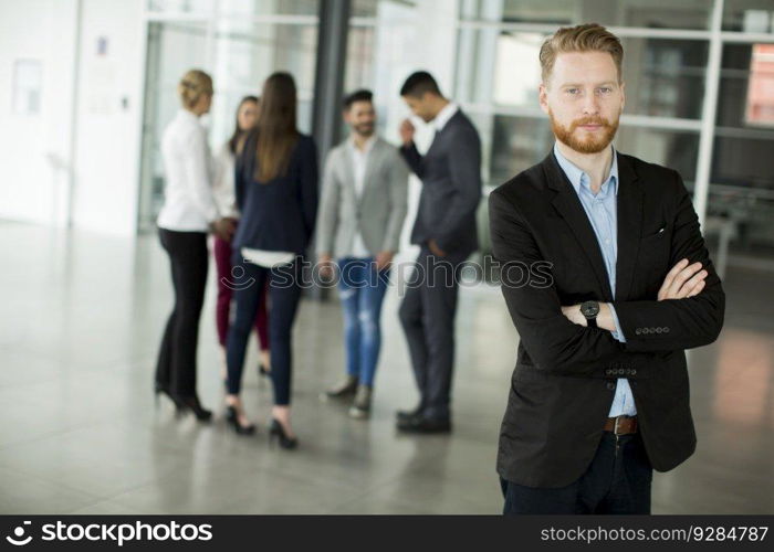 Businessman standing in the office and other business people talking at background