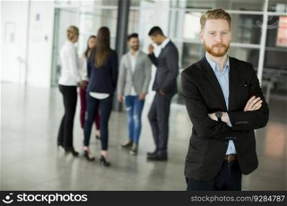 Businessman standing in the office and other business people talking at background