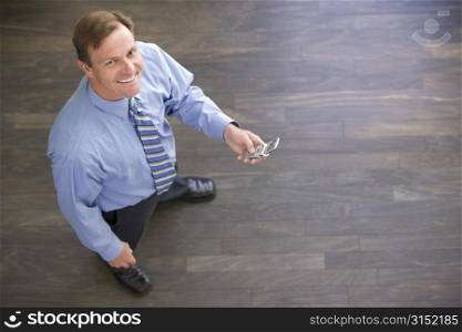 Businessman standing indoors holding cellular phone smiling
