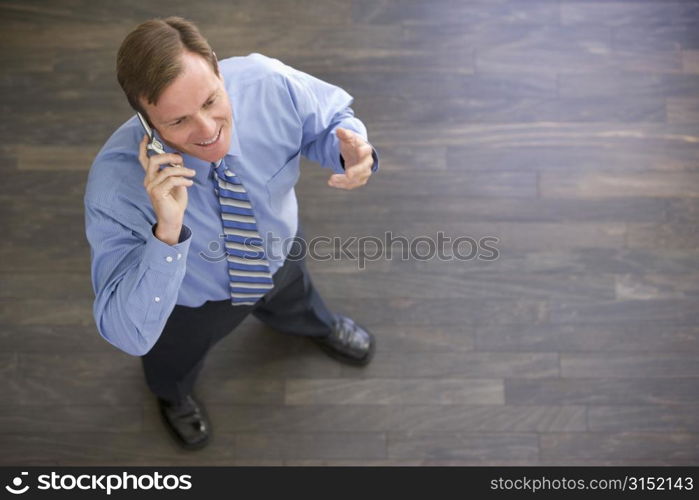 Businessman standing indoors using cellular phone and smiling