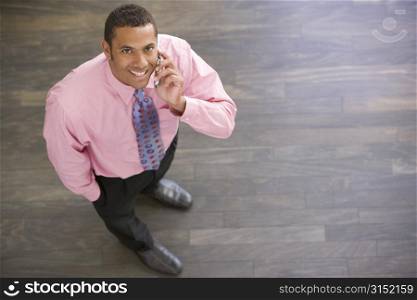 Businessman standing indoors using cellular phone smiling