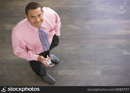 Businessman standing indoors with cellular phone smiling