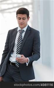 Businessman standing inside modern office building looking on a mobile phone