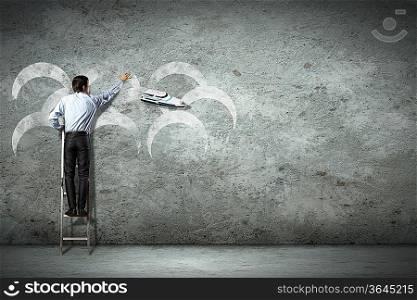 Businessman standing on ladder and pointing on picture on wall
