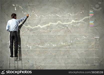 businessman standing on ladder drawing diagrams and graphs