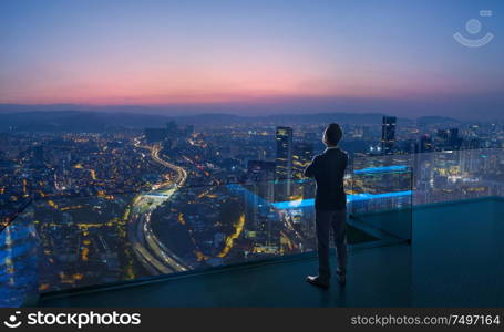 Businessman standing on open roof top balcony watching city night view . Business ambition and vision concept .