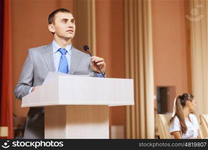 Businessman standing on stage and reporting for audience. Speaker at stage