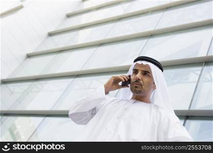 Businessman standing outdoors by building on cellular phone (selective focus)