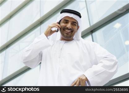 Businessman standing outdoors by building on cellular phone smiling (selective focus)