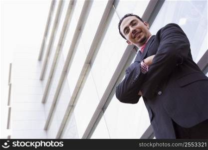 Businessman standing outdoors by building smiling (high key/selective focus)