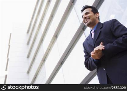 Businessman standing outdoors by building smiling (high key/selective focus)