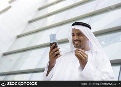 Businessman standing outdoors by building using personal digital assistant and smiling (selective focus)