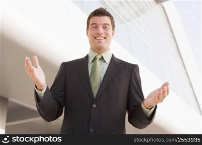 Businessman standing outdoors by building with hands out