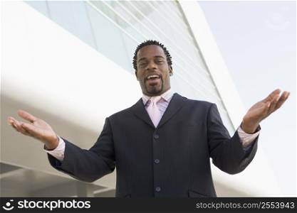 Businessman standing outdoors by building with hands out smiling