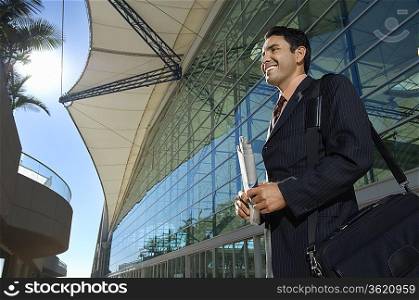 Businessman standing outside office building and smiling, low angle view