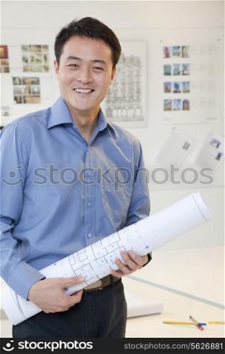 Businessman standing with stuck of papers in the office, portrait